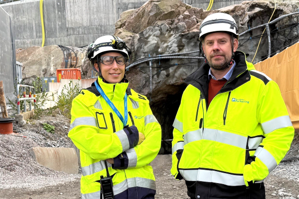 Vd samt projektchef i varselkläder och bygghjälm framför Hjorthagsberget